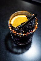 Un vaso con una bebida oscura, una rodaja de naranja y una pajita, decorado con ralladura de naranja.