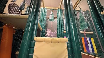 Espaço infantil coberto com estrutura de escalada, paredes acolchoadas e teto em rede.