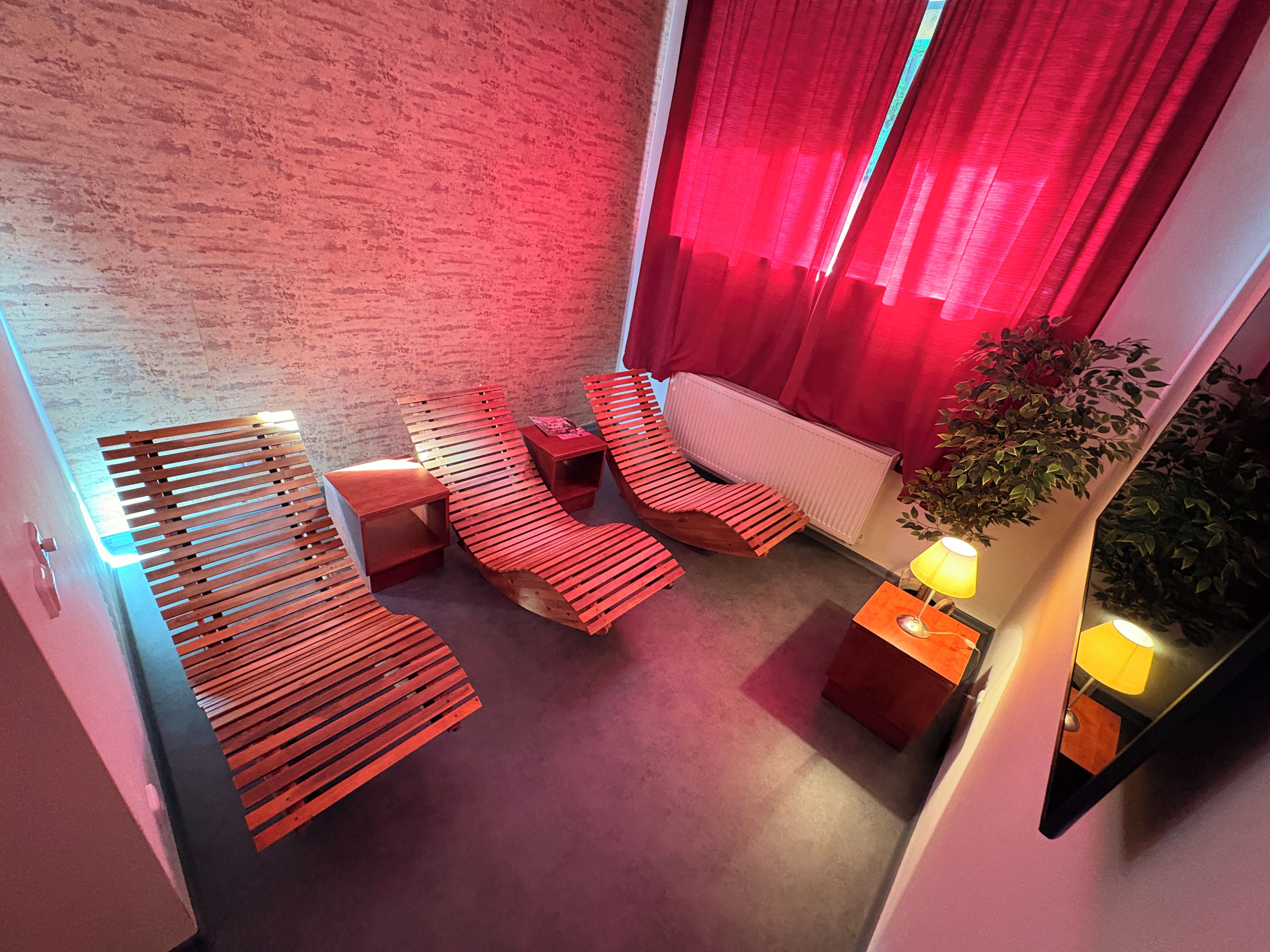Un interior moderno con una habitación iluminada en rojo, un sofá, una silla, una mesita y una planta en maceta.