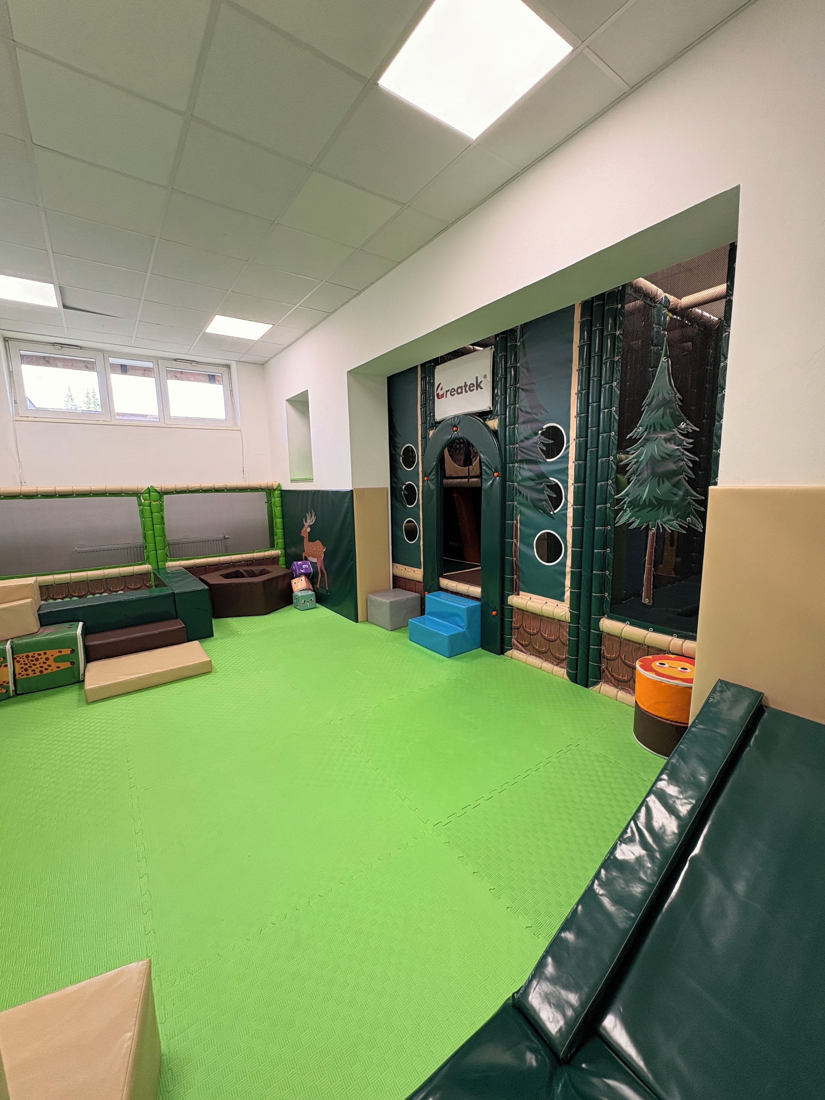 Espaço de recreação com piso verde, casinha e janela.