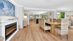 A spacious dining area with a long wooden table and wicker chairs, a fireplace with a modern design, and a large abstract painting on the wall. - ChrisTony 5 Bdrm Waterfrnt Cottage (Lake Munmorah)