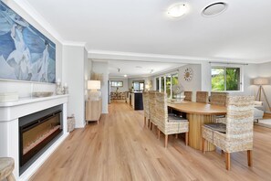 Ein geräumiger Essbereich mit einem langen Holztisch, Korbstühlen, einem modernen Kamin und einem großen abstrakten Gemälde an der Wand.