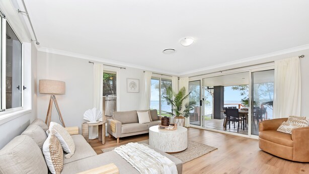 A spacious living room with a sofa, a coffee table, and a view of the outdoors. - ChrisTony 5 Bdrm Waterfrnt Cottage (Lake Munmorah)