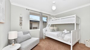 A bedroom with a bunk bed, a sofa, a lamp, and a window with curtains. - ChrisTony 5 Bdrm Waterfrnt Cottage (Lake Munmorah)
