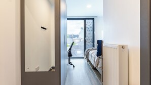 Ein schmales Entree mit einem Bett auf der rechten Seite, einem Heizkörper und einer Tür links.