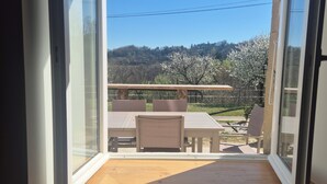 Vista a través de un ventanal hacia un balcón con piso de madera, una mesa y sillas.