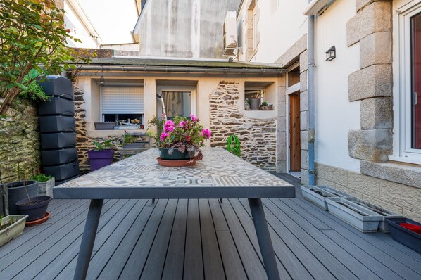 A wooden deck with a table, potted plants, and a stone wall.