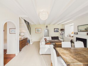 A spacious living room with a white sofa, a wooden coffee table, and a fireplace. A staircase leads to an upper level, and there are framed pictures on the walls. - House for 8 with garden and river view (La Trinité-sur-Mer)