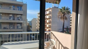 A balcony with a table and chairs, overlooking a street with buildings and a palm tree. - Studio 30 meters from the beach, Saint Raphaël, near TGV station and town center, parking. (Saint-Raphaël)