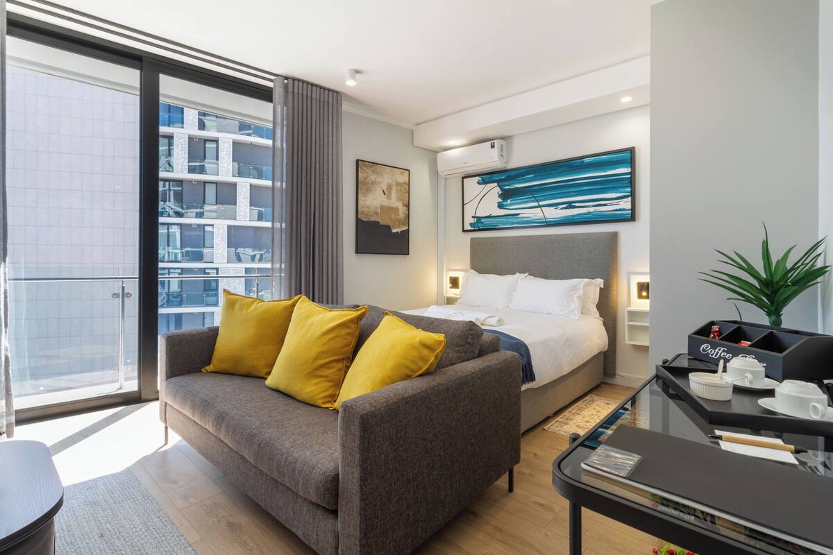 A modern hotel room with a sofa, bed, and a glass table with coffee cups.