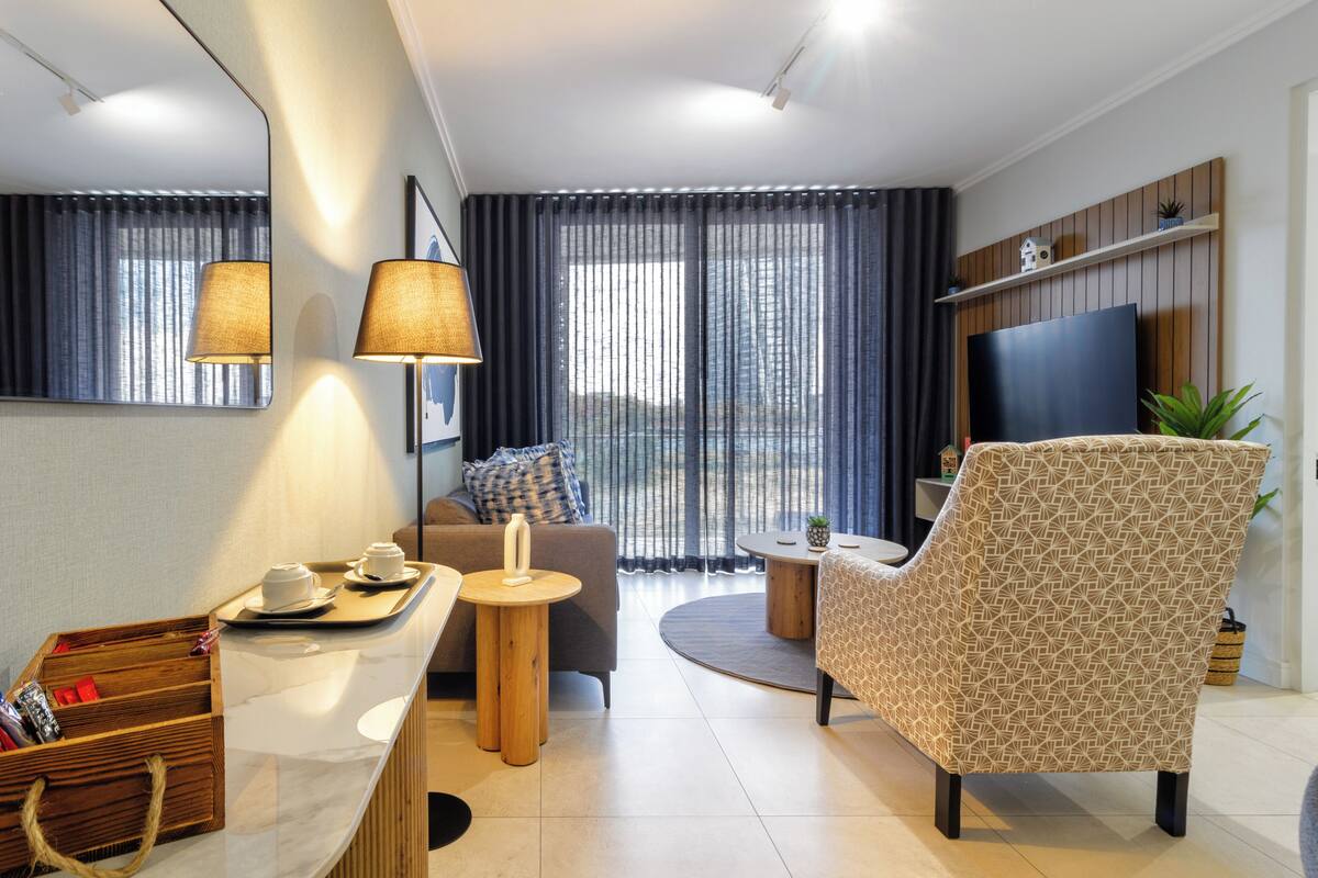 A modern living room with a sofa, armchair, TV, and a small table with a tray of items.