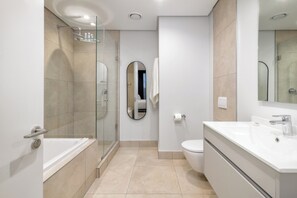 Un baño moderno con ducha de vidrio, inodoro, lavabo y espejo.