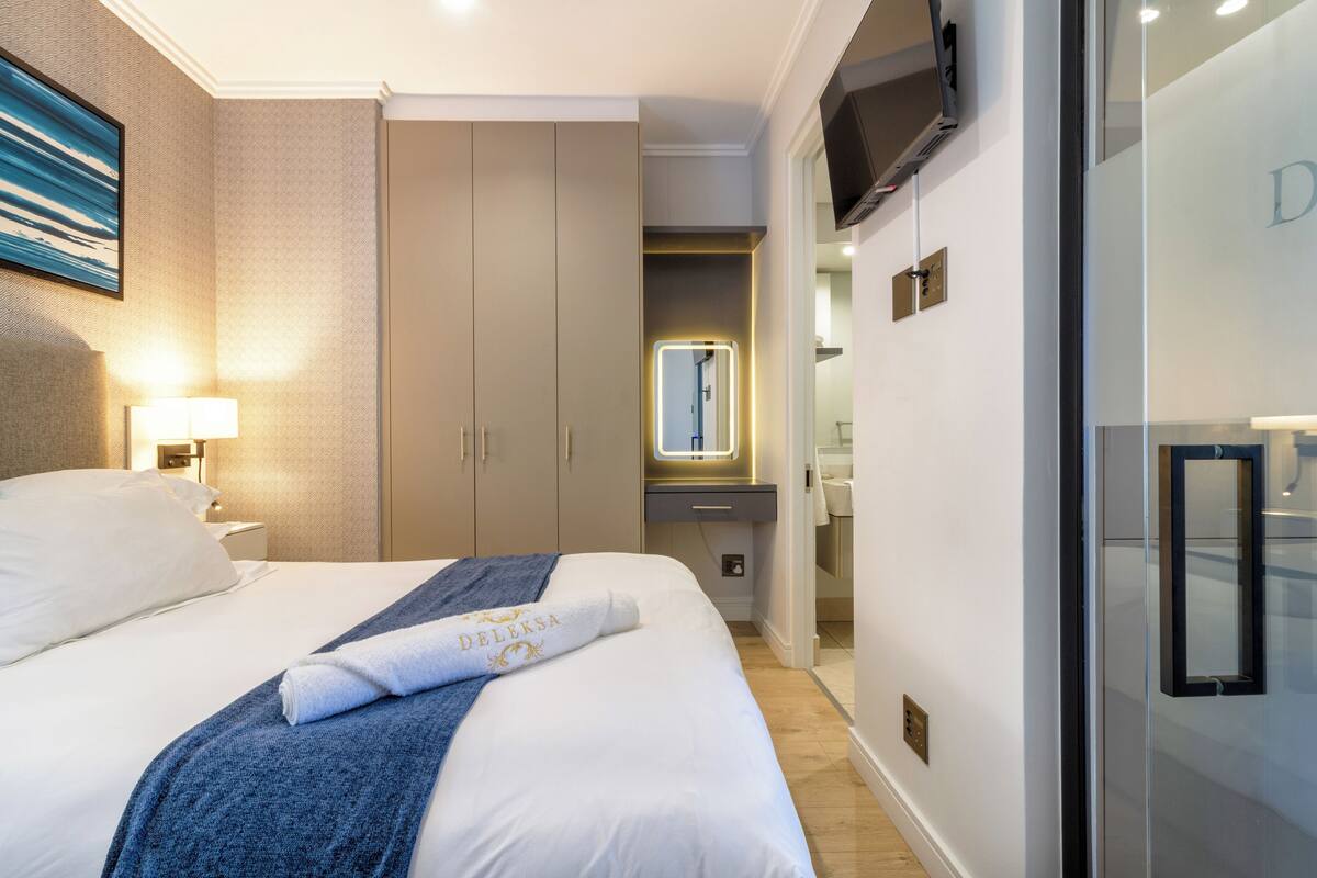 A hotel room with a bed, a nightstand, a lamp, a wardrobe, a mirror, and a television.