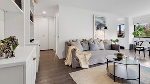 Ein modernes Wohnzimmer mit einem grauen Sofa, einem Glastisch und einer weißen Ablagetisch mit Dekoration.