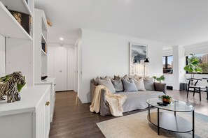 Ein modernes Wohnzimmer mit einem grauen Sofa, einem Glastisch und einer weißen Ablagetisch mit Dekoration.