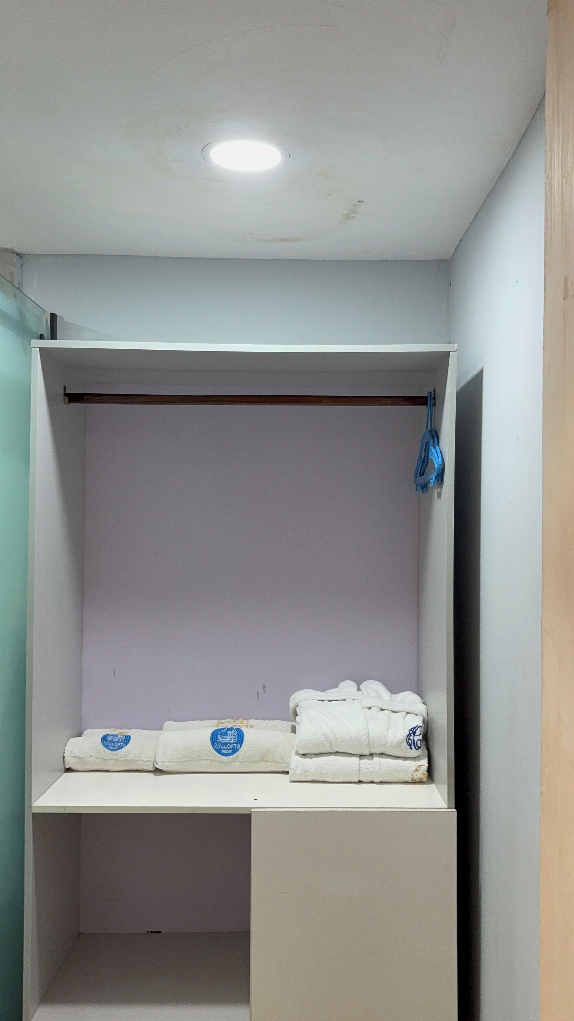 Een kleine, afgesloten kamer met een bed, een plank en een blauw hangend object.