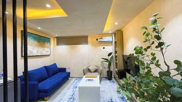 A modern living room with a blue sofa, a white coffee table, and a large green plant.
