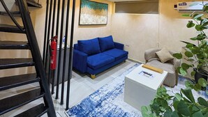 Una sala moderna con un sofá azul, una mesa de centro blanca y una escalera con barandillas negras.