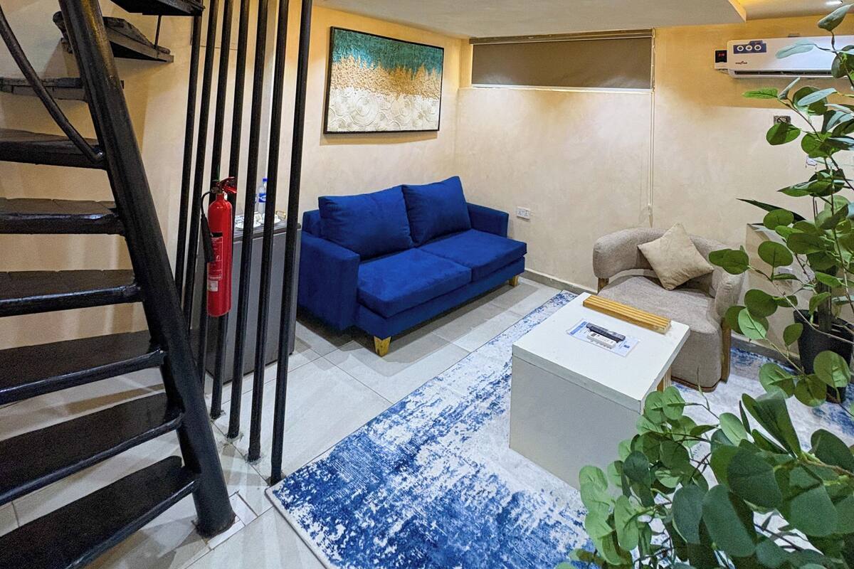 A modern living room with a blue sofa, a white coffee table, and a staircase with black railings.