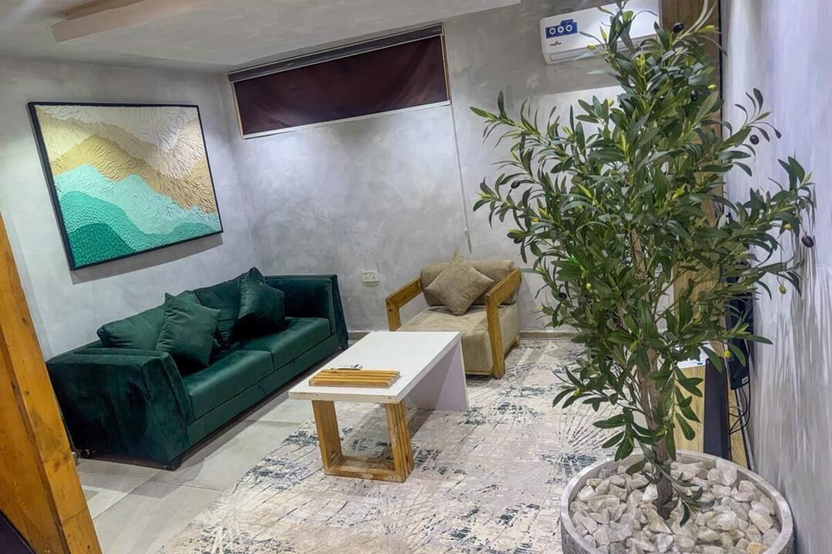 A living room with a green sofa, a white coffee table, a potted plant, and a painting on the wall.