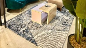 Una sala de estar moderna con un sofá azul verdoso, un sillón color beige, una mesa de centro de madera y una planta verde grande.