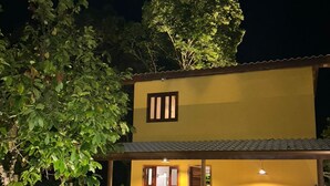 Ein zweistöckiges Haus mit gelber Fassade, einer überdachten Veranda und einem großen Baum im Hintergrund.
