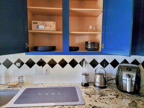 A kitchen with blue cabinets, a black and white tiled backsplash, a countertop with a kettle, a toaster, and a box of cleaning sponges. - Entire house/Large TVs in all rooms/ Massage Chair/Gym/Grill (Houston)