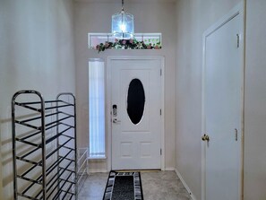 A hallway with a white door, a metal rack, a small window with blinds, and a decorative garland above the door. - Entire house/Large TVs in all rooms/ Massage Chair/Gym/Grill (Houston)