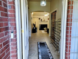 Un couloir avec une porte à gauche, un portail en métal à droite, une cheminée au centre et un ventilateur de plafond au-dessus.