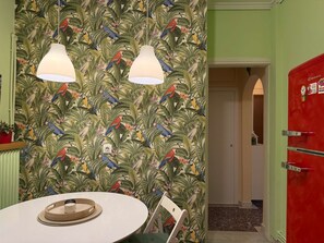 Ein Zimmer mit tropischer Vogel-Tapete, einem weißen Tisch mit Tablett und einem roten Schrank.