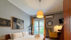 A bedroom with a bed, a desk, a chair, a TV, and a window with a view of the outside. - Miró by halu! - Cozy apartment on Mitropoleos street (Thessaloniki)