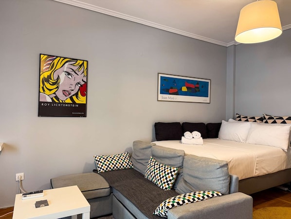 Una camera d'albergo moderna con un divano grigio, un letto con lenzuola bianche e due opere d'arte alle pareti.