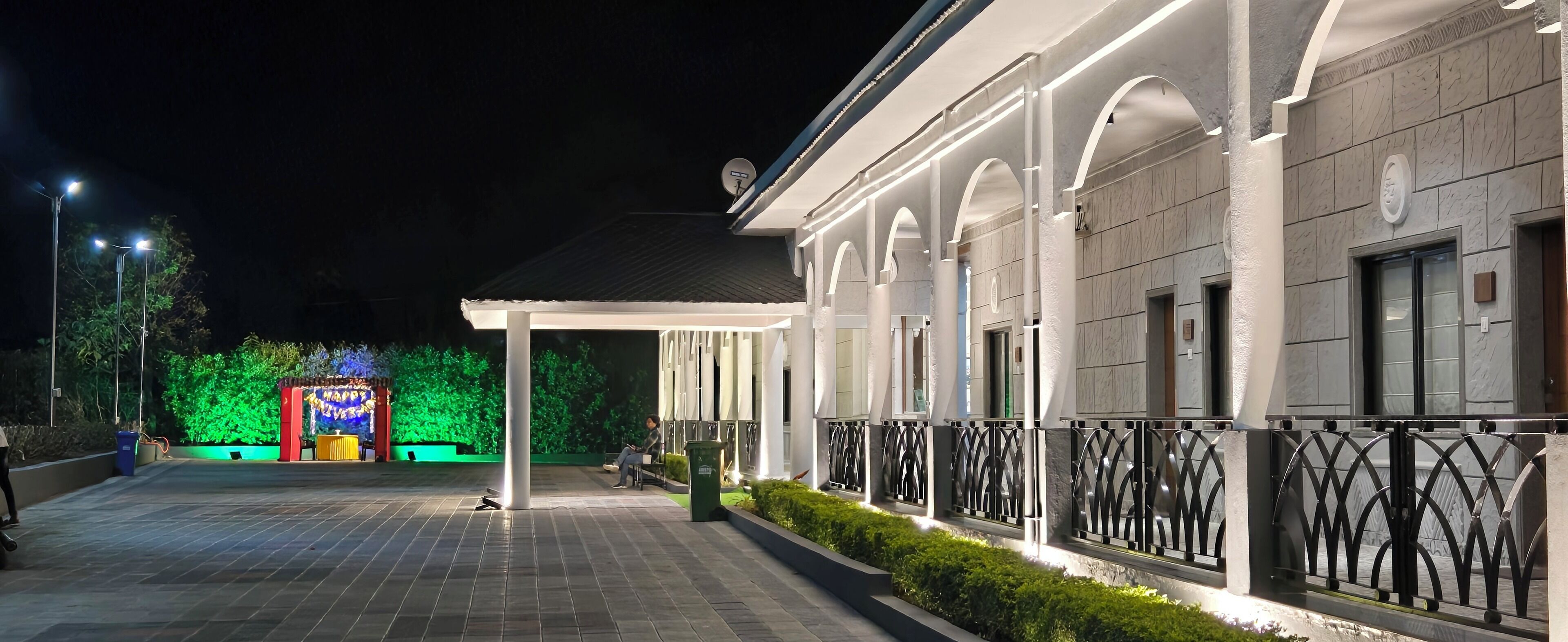A well-lit outdoor area with a covered walkway, a green-lit structure in the background, and a security fence.