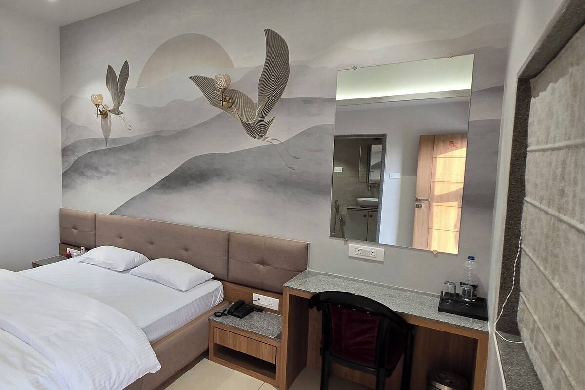 Une chambre d’hôtel équipée d’un lit, d’un bureau, d’une chaise, d’un miroir et d’un climatiseur fixé au mur.