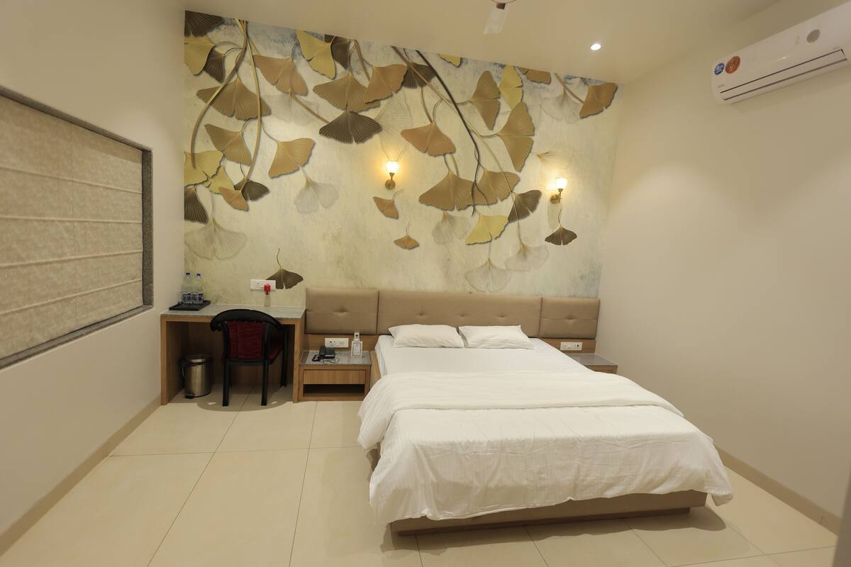 Une chambre à coucher avec un lit, un bureau et une chaise. Il y a un élément décoratif sur le mur et un appareil de climatisation.
