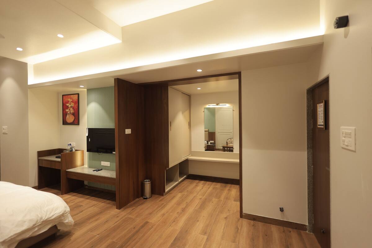 Une chambre d’hôtel avec un lit, un bureau, un miroir et une salle de bain visible à travers une porte ouverte.