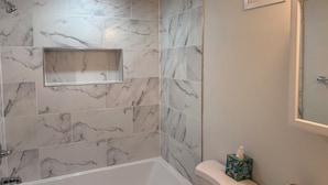 A bathroom with a bathtub, toilet, and a shelf with a tissue box. - 2 bedrooms basement apartment (Washington)