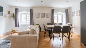 A modern living room with a sofa, a dining table with chairs, and a kitchen area. - Large Maisonette 90 m² | For Groups | 9 Guests (Kapfenberg)