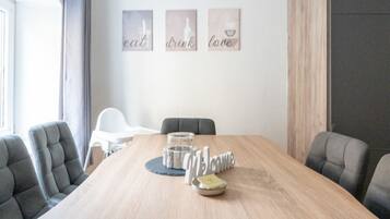 A conference room with a wooden table, four grey chairs, a white chair, and three wall art pieces with the words "eat," "drink," and "love."