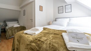 A hotel room with two beds, one with a gold blanket and the other with white bedding. There are towels on the beds and a discount voucher on the bed with the gold blanket. - Large Maisonette 90 m² | For Groups | 9 Guests (Kapfenberg)