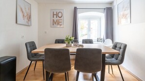 A modern dining area with a wooden table, four grey upholstered chairs, and a "Welcome" sign. - Large, Quiet Maisonette for 10 | 24/7 Check-in (Kapfenberg)