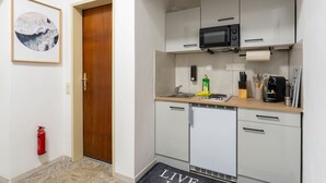 Eine kleine Küche mit Mikrowelle, Spüle und Kaffeemaschine. Ein Feuerlöscher ist an der Wand angebracht und über der Tür hängt ein gerahmtes Bild.