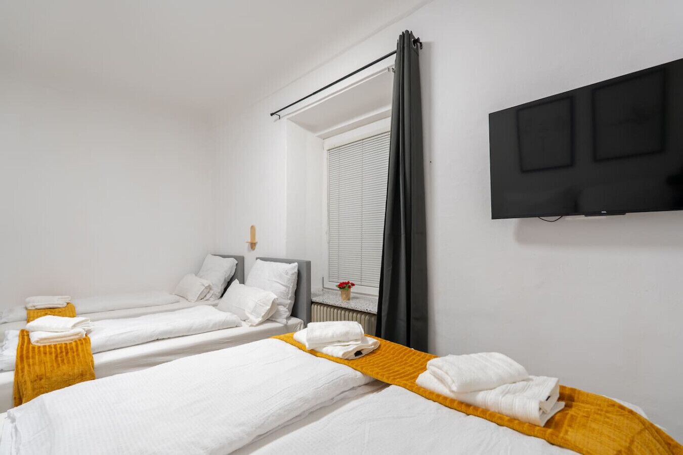 Habitación de hotel con dos camas individuales, un televisor montado en la pared y una ventana con persianas.