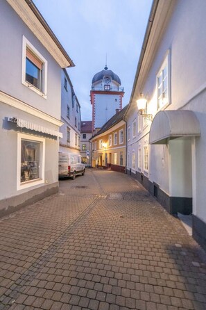 Une rue pavée bordée de bâtiments des deux côtés, un beffroi en arrière-plan et un fourgon garé.