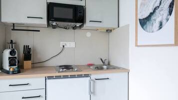 A compact kitchen with white cabinets, a microwave, a toaster, and a sink. There is a fire extinguisher on the floor.