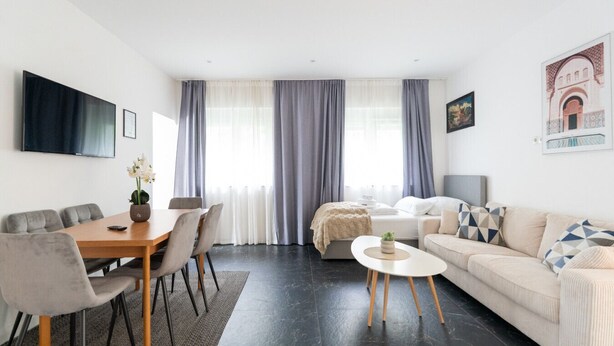 A modern living room with a dining area, a sofa, a coffee table, and a TV mounted on the wall. - Near Vienna•60m²•6 Guests• Self Check-in & Parking (Purkersdorf)