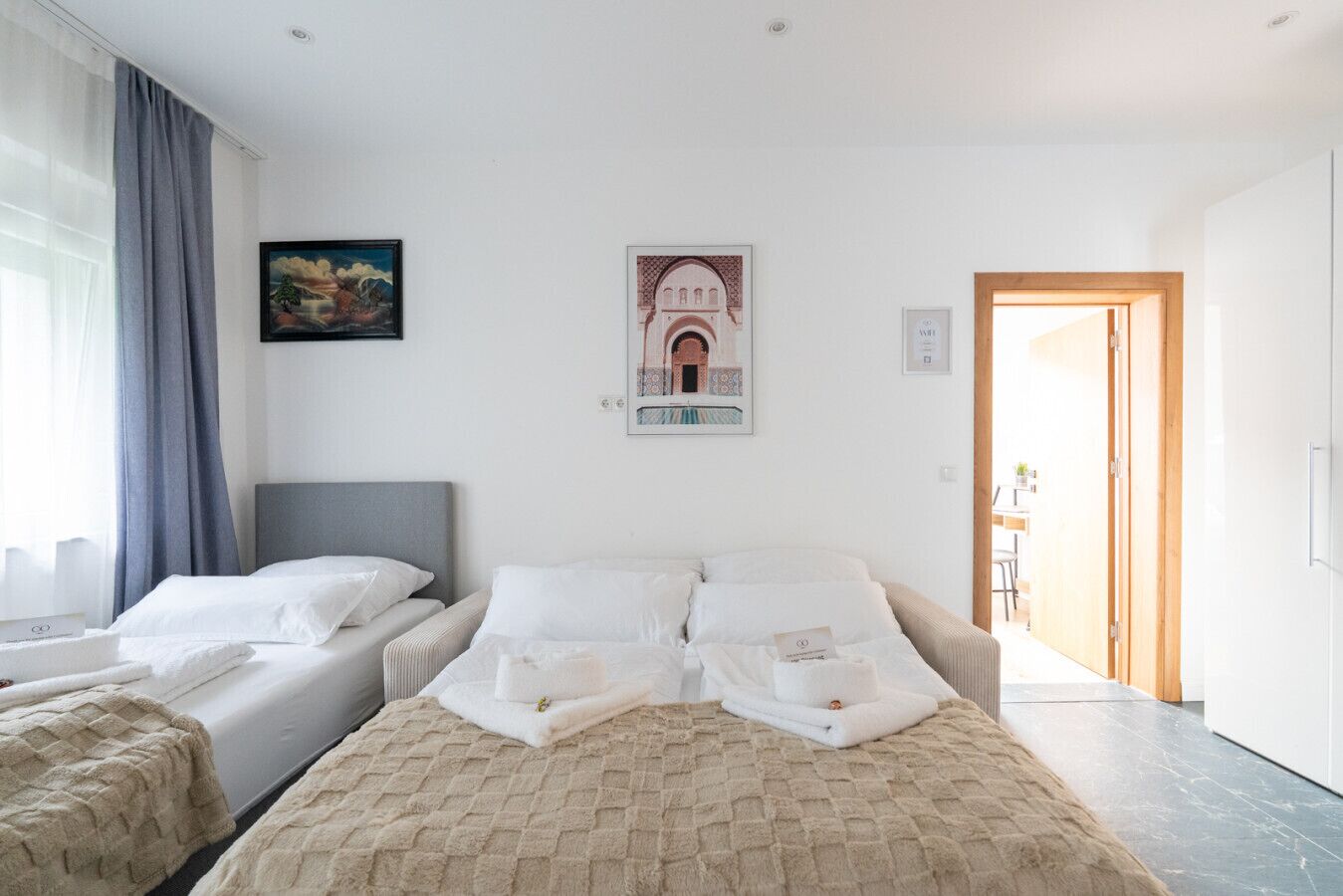 Ett hotellrum med en säng, en soffa och ett skrivbord. Det finns en tavla på väggen och en dörr som leder till ett annat rum.