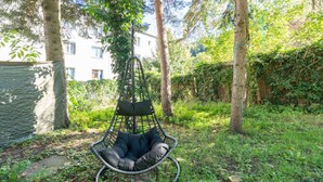 A hanging chair in a lush garden with trees and a building in the background. - Near Vienna•60m²•6 Guests• Self Check-in & Parking (Purkersdorf)