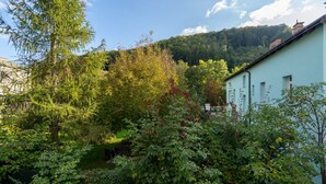 A lush garden with dense foliage and a light blue building with a sloped roof. - 60m² Apt • Business & Family Ready • Near Vienna (Purkersdorf)