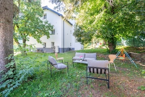 Un espace jardin aménagé avec du mobilier d’extérieur, une balançoire et un bâtiment en arrière-plan.